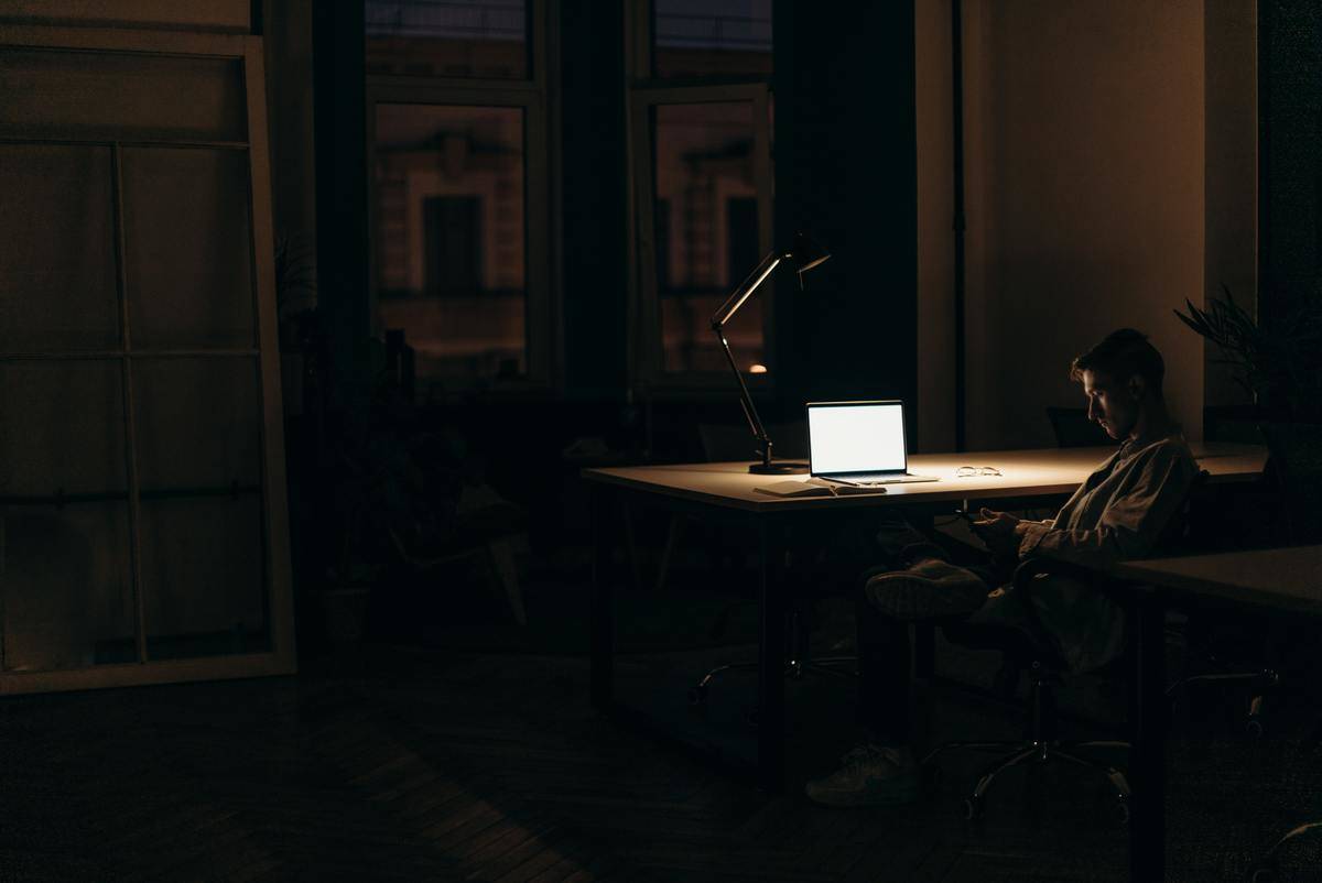 A man sitting at his laptop at a desk in the middle of the night.