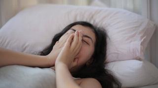 A woman asleep in bed, her hands covering her mouth.