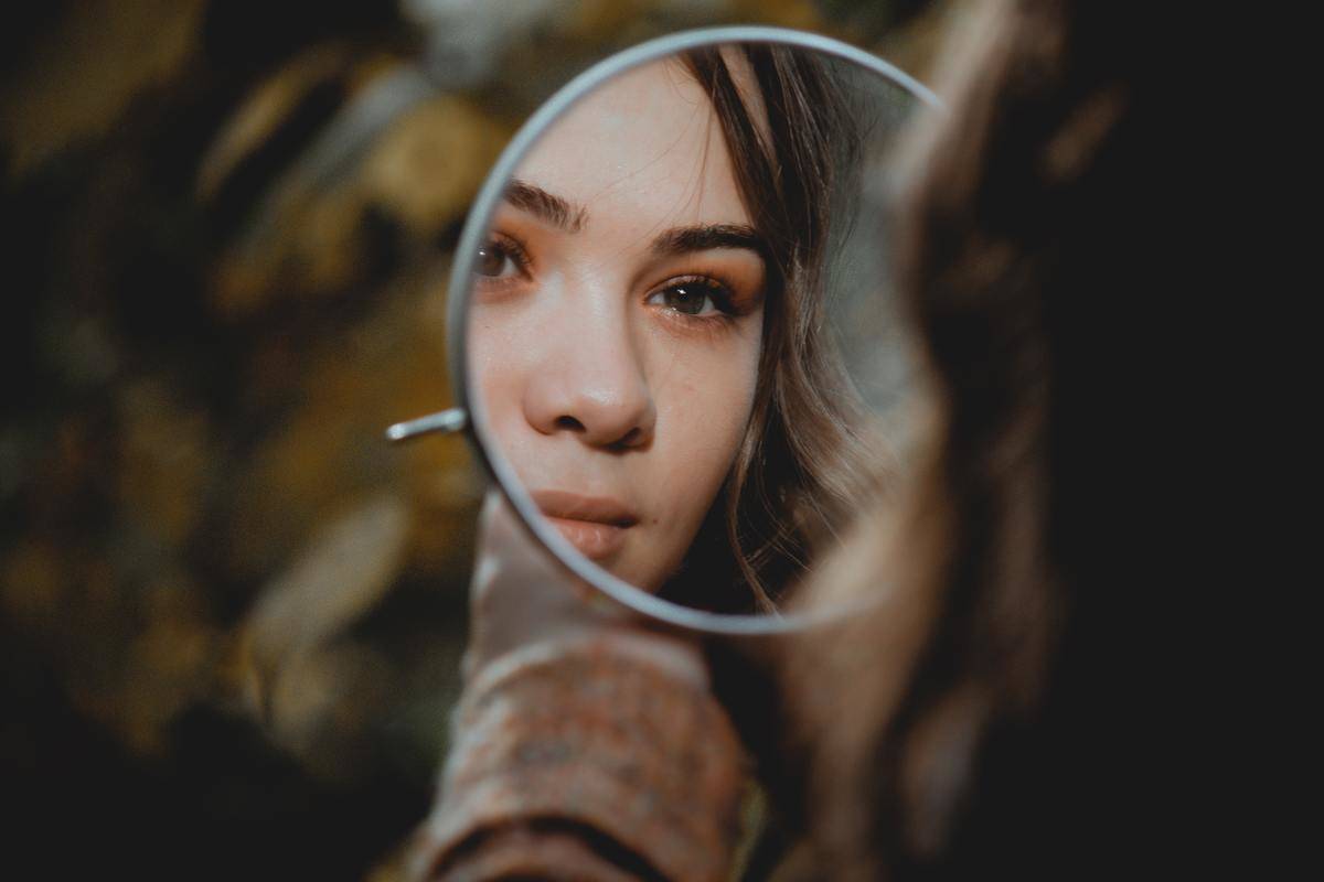 A woman looking at a reflection of herself in a small mirror.