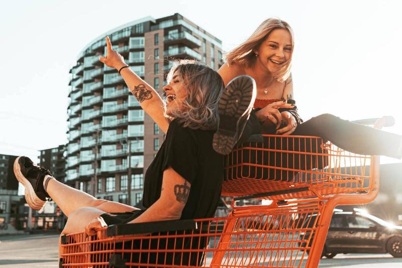 Two friends laughing as they ride together in a shopping cart.