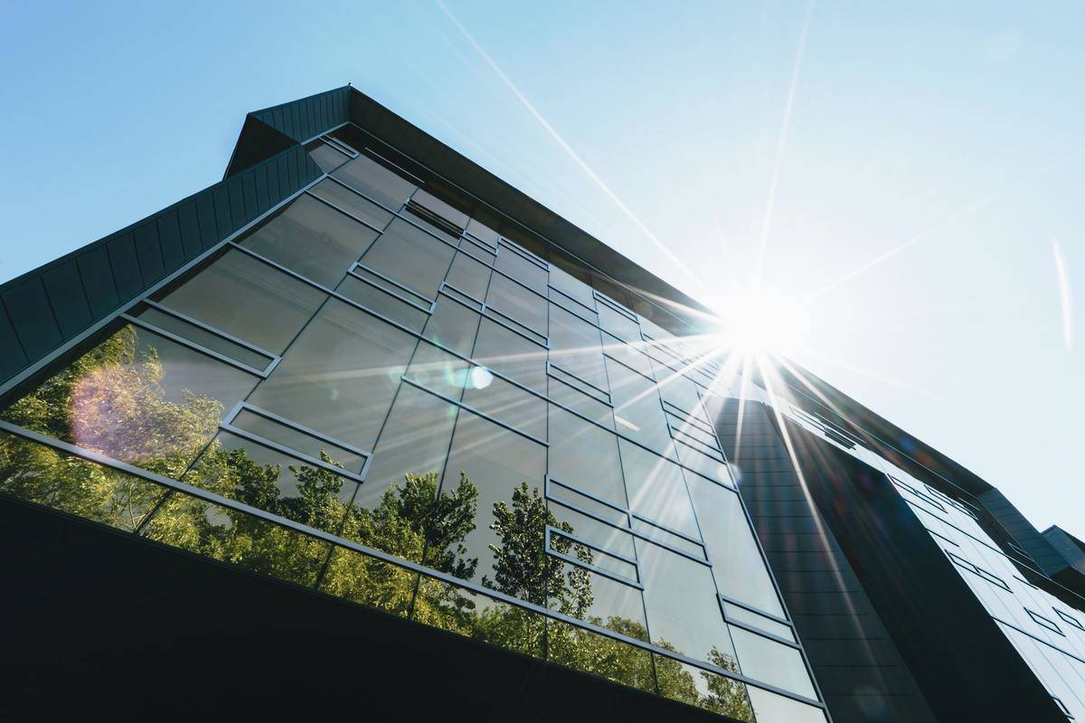 A futuristic building with a completely windowed wall, show from below, the sun cresting over the edge of the roof.