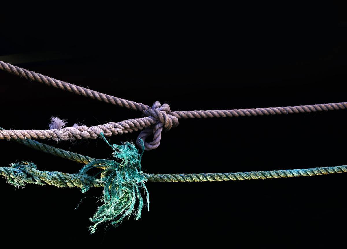A purple and teal string rope against a black background, both featuring frayed knots.