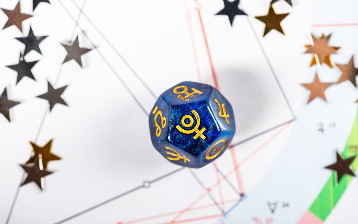 A dice with the symbol for Pluto on its face atop a star chart.