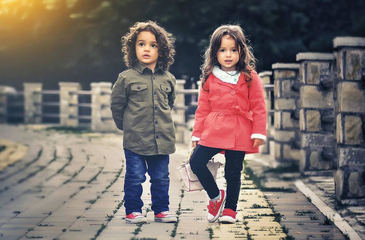 two-children-standing-near-concrete-fence