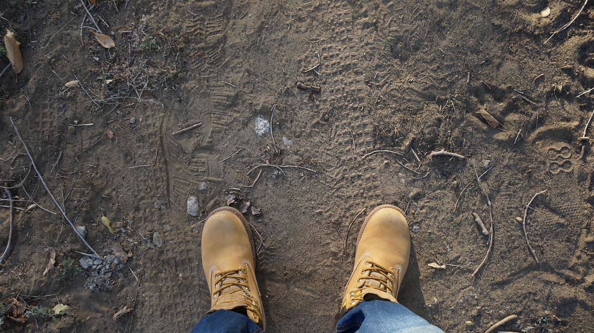 Someone standing on a dirt path, the camera angled down at their boots.