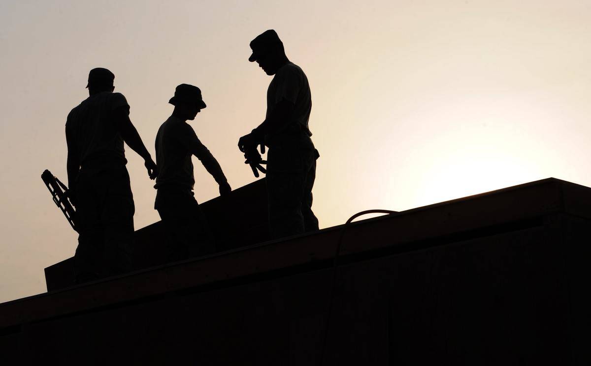 A silhouette of three workers on a roof.