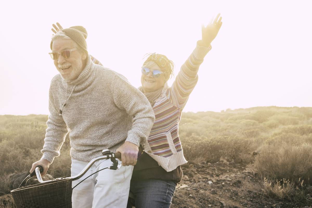 Two seniors on a bike, laughing, one with her arms in the air.