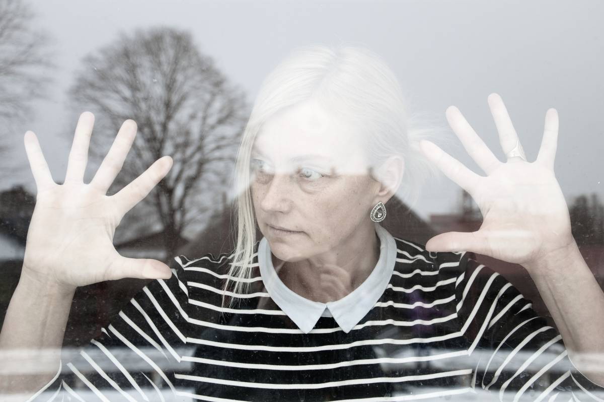 Woman in isolation behind the window, hands pressed against the glass.