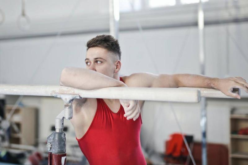 A male gymnast leaning against some bars.