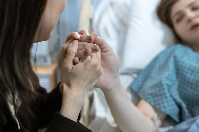 A woman holding a loved one's hand as they lay in a hospital bed.