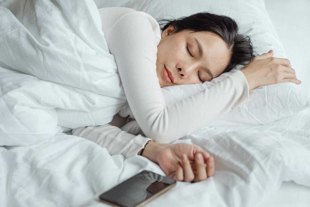 A woman sleeping on white sheets, a phone next to her hand.
