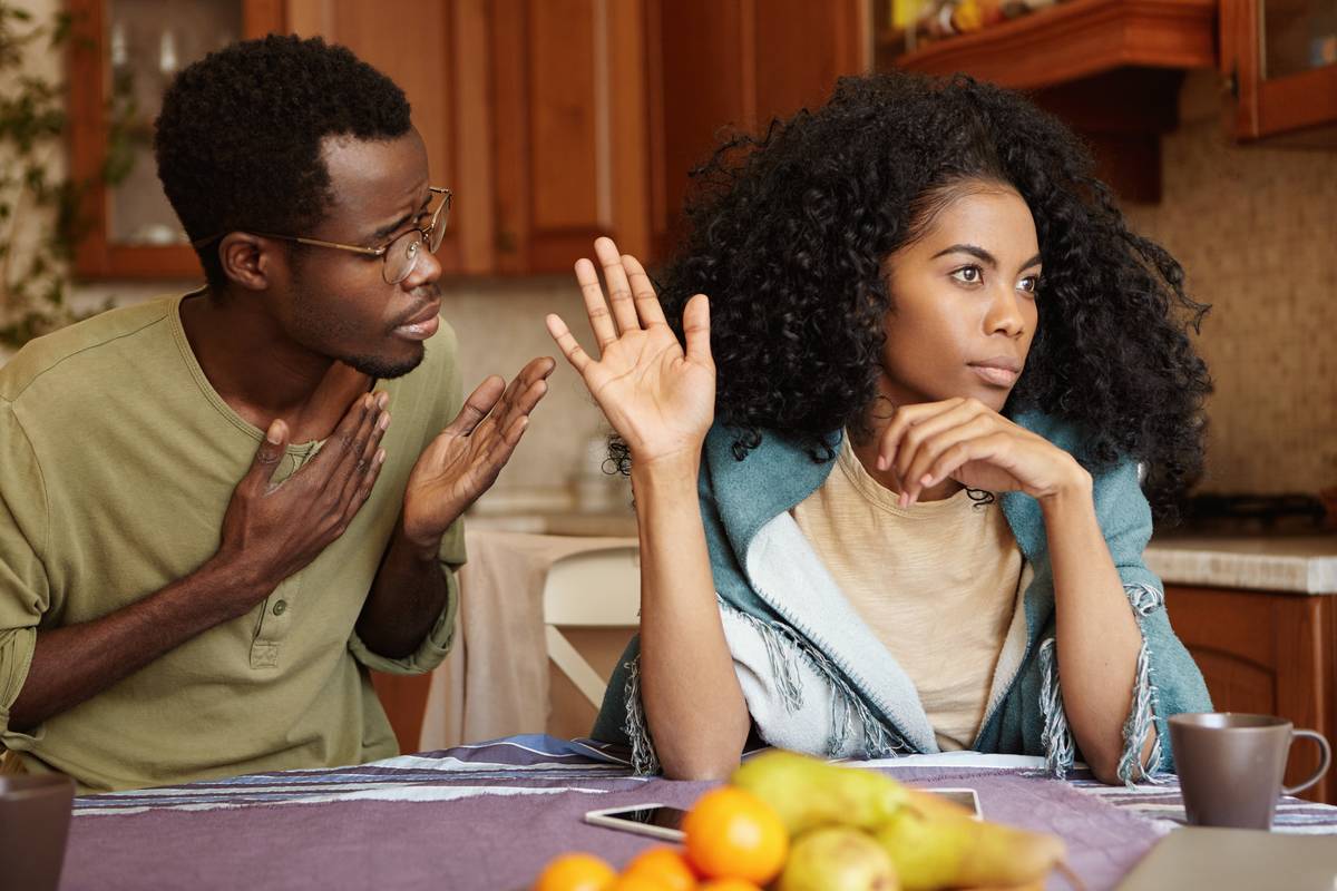 Unhappy African American male cheater holding hand on his chest apologizing to beautiful indifferent woman who ignoring and refusing all his excuses, telling him to get lost.