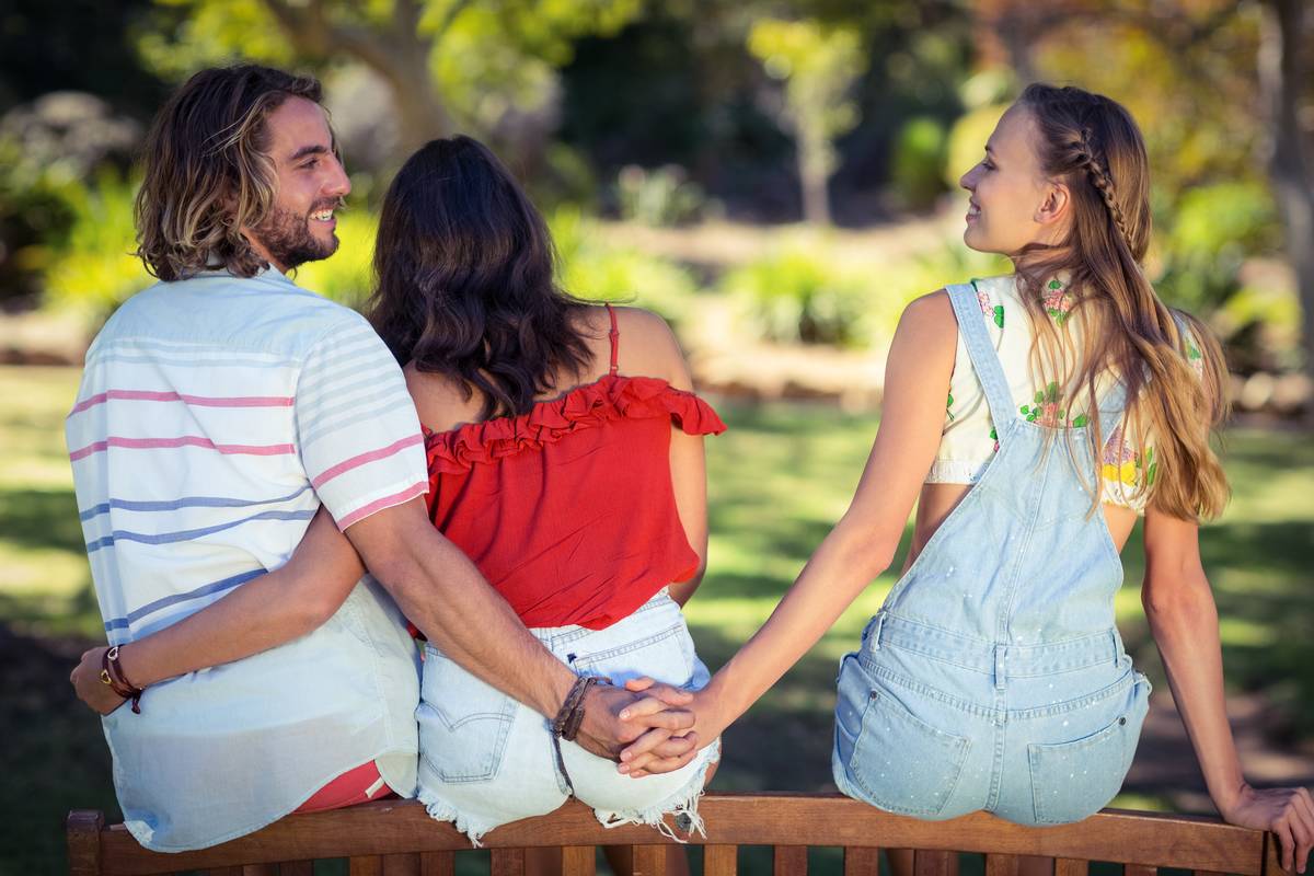 A man holding another woman's hand behind his girlfriend's back.