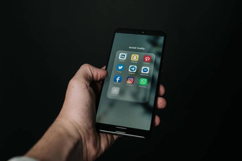 A hand holding up a phone, displaying a folder of social media apps.