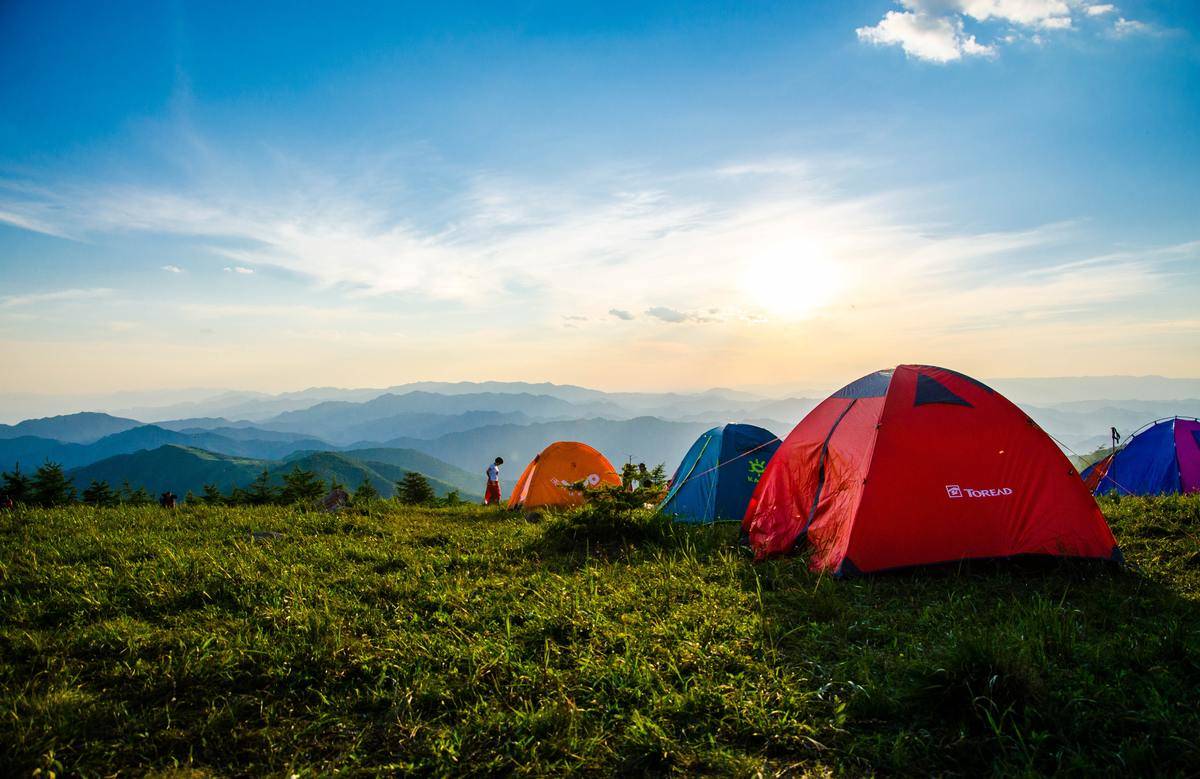 A group of tents pitched in a field along a mountain range.
