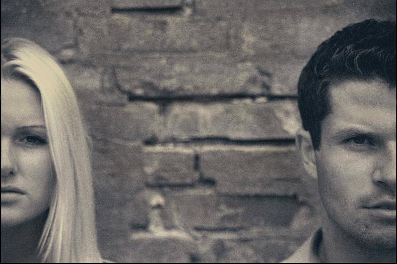 A greyscale image of a couple, standing a few feet away, each of their faces cut off by the photo.