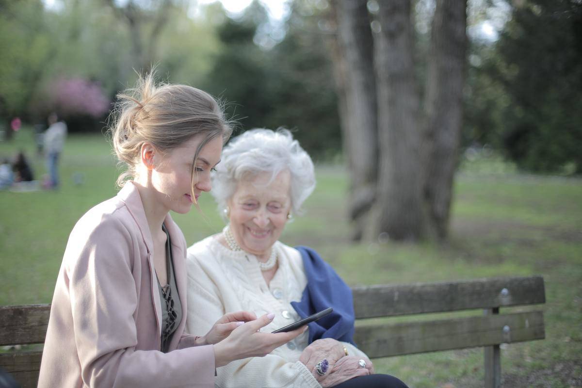 A woman seated next to her older mother, showing her something on her phone.