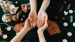 Someone getting both their palms read over a table with tarot cards and crystals.
