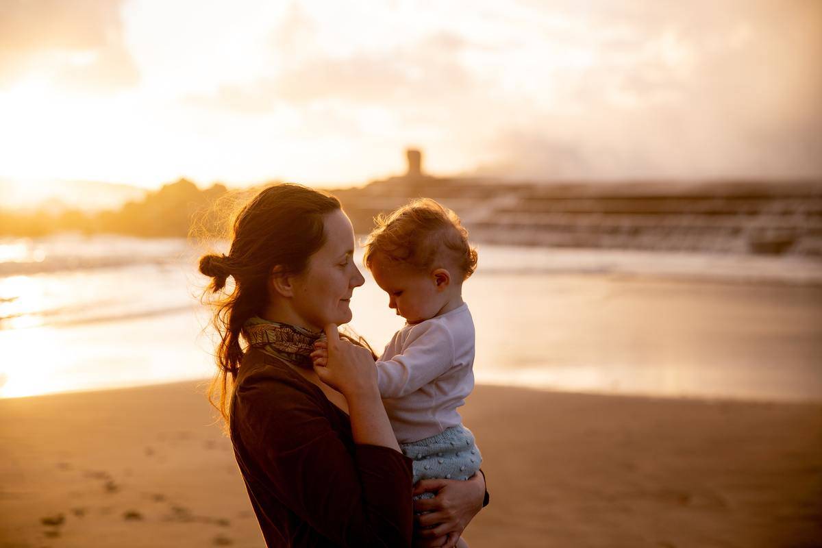A woman holding her baby on the beach.