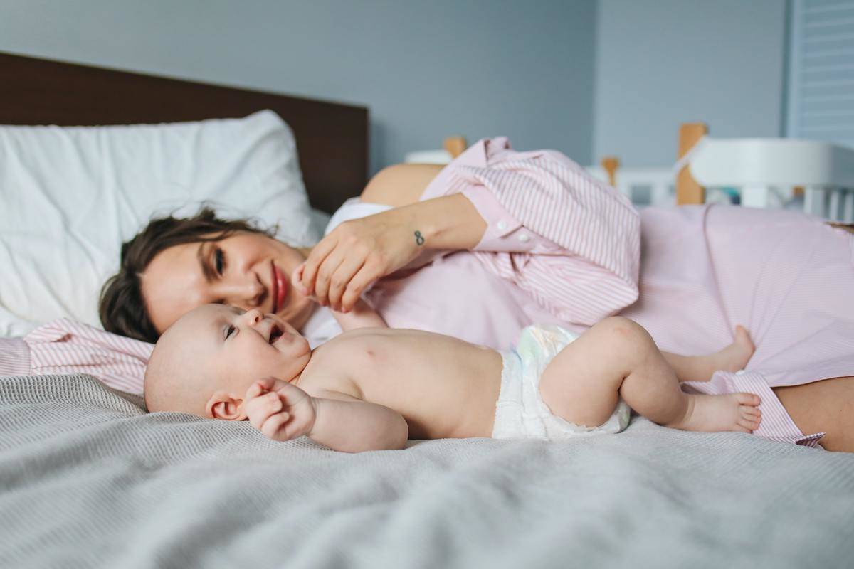 A woman laying in bed next to her baby.