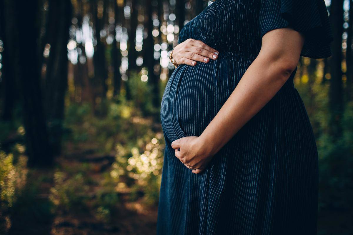 A woman standing outside cradling her pregnant stomach.