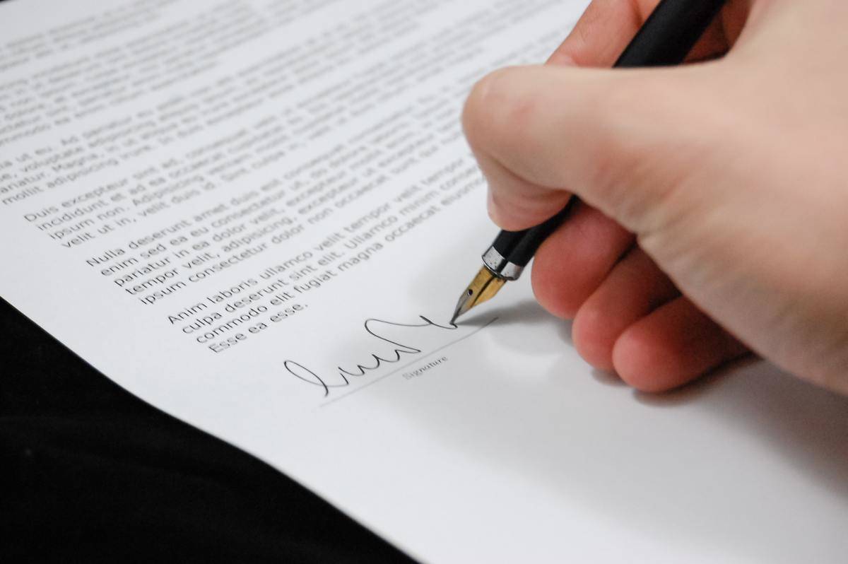 A hand signing a legal document with a fountain pen.