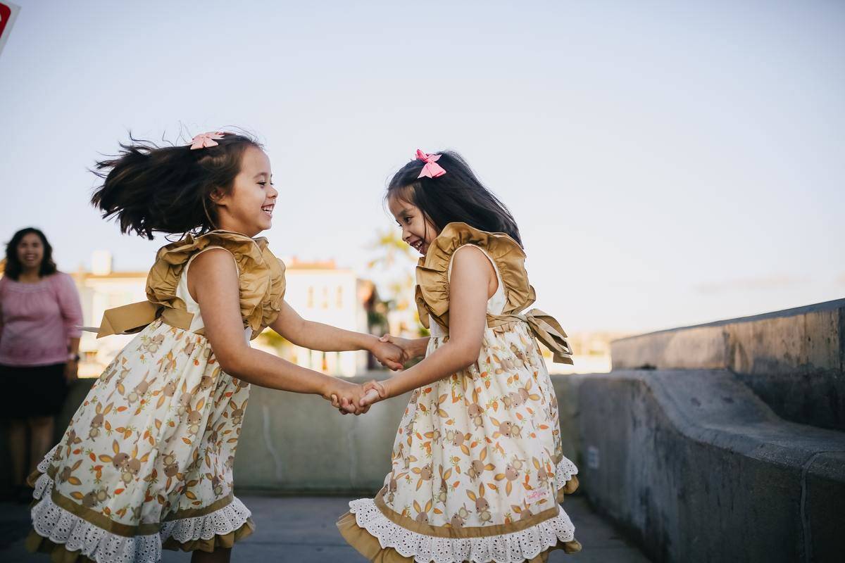 Two twin girls in matching dresses, spinning and dancing together.