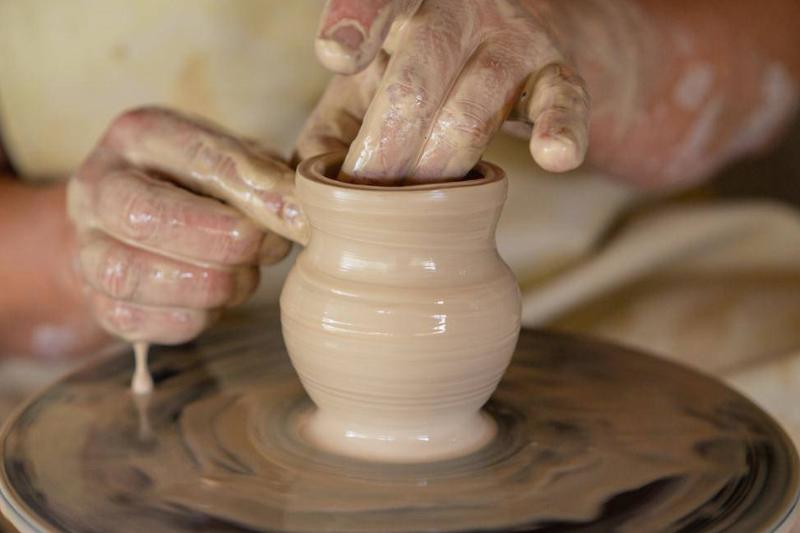 A closeup of someone's hands as they form a small vase on a pottery wheel.