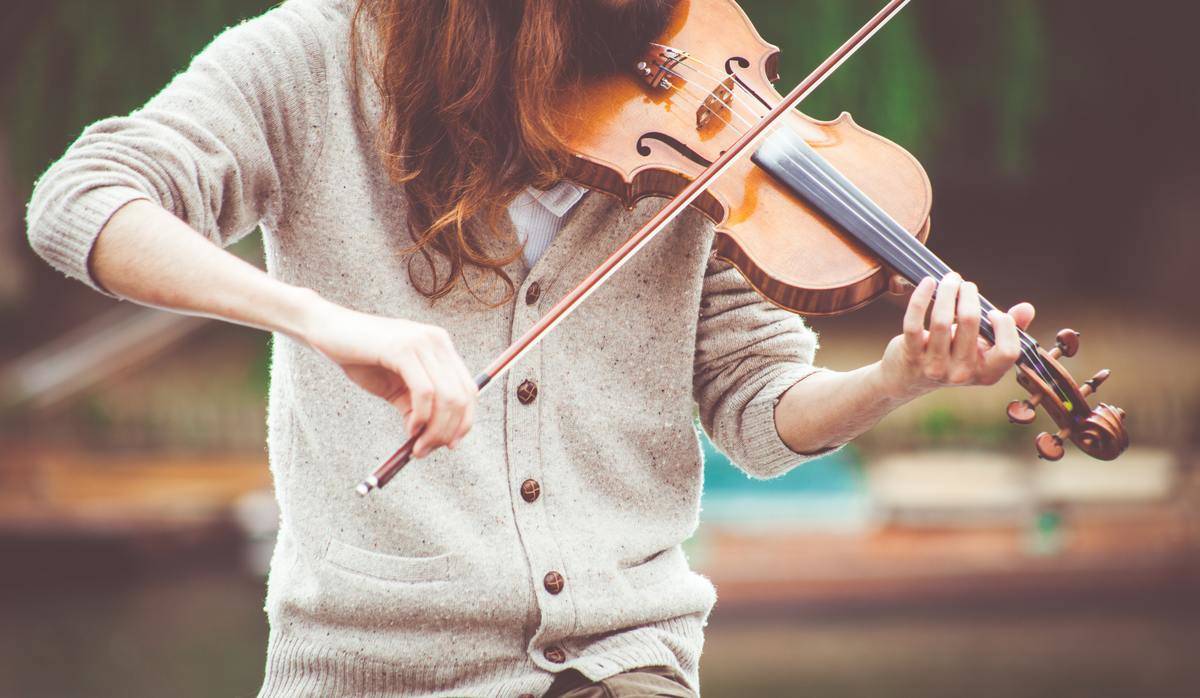 A woman in a grey cardigan playing the violin.