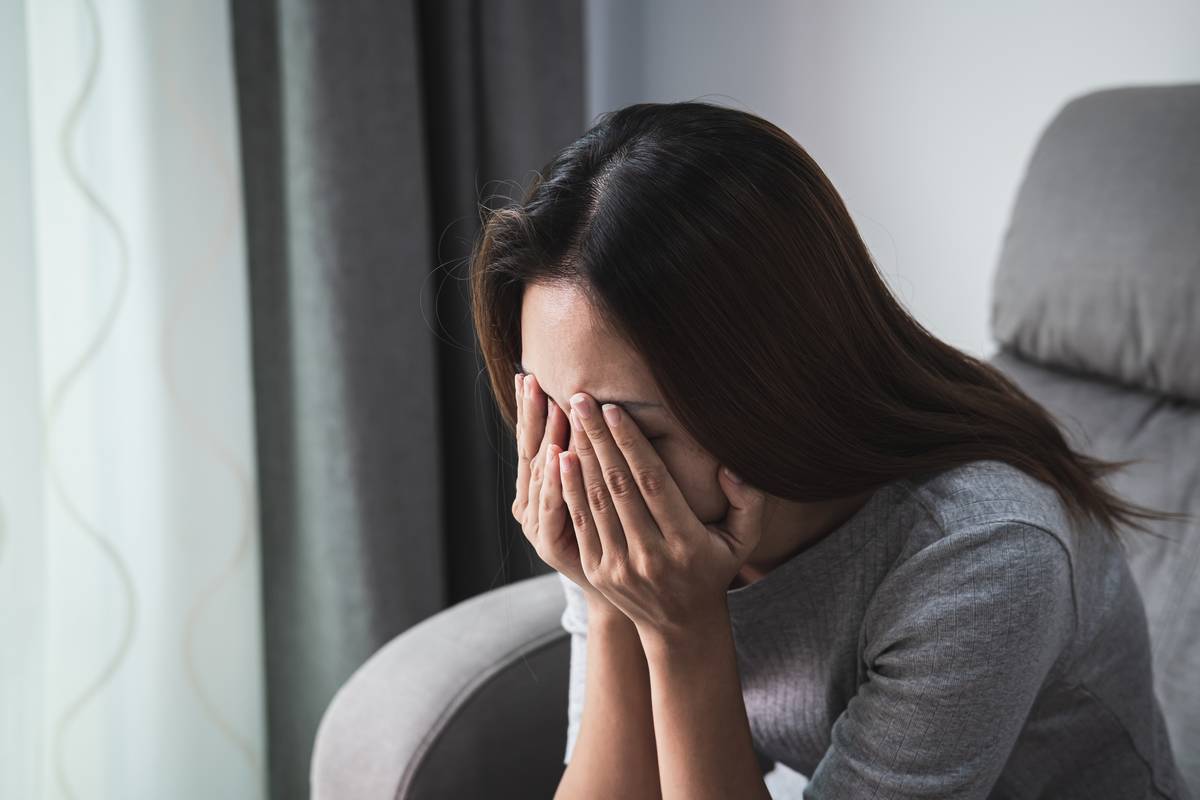 A sad woman sitting on a chair, her face in her hands.