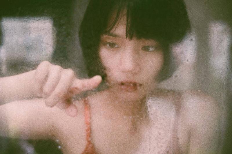 A girl looking through a rain-covered window, her finger up against it.