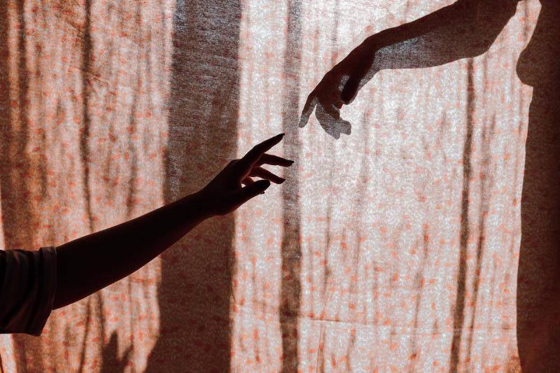 Two hands reaching out for each other, one in front of a curtain and one behind.
