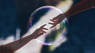 Two hands reaching out for each other, semi-transparent, in front of an image of a bubble.