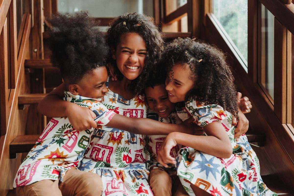 A group of young siblings hugging on a set of steps, all in matching shirts/dresses.