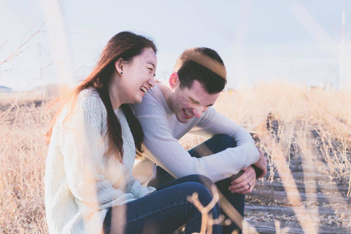 A couple sitting along a path in a field, laughing.