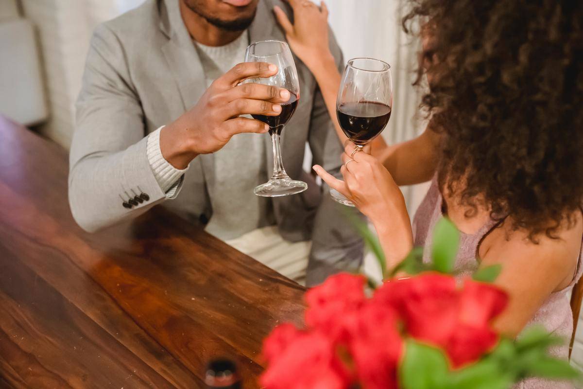 A couple drinking wine at home, both seated at a table.