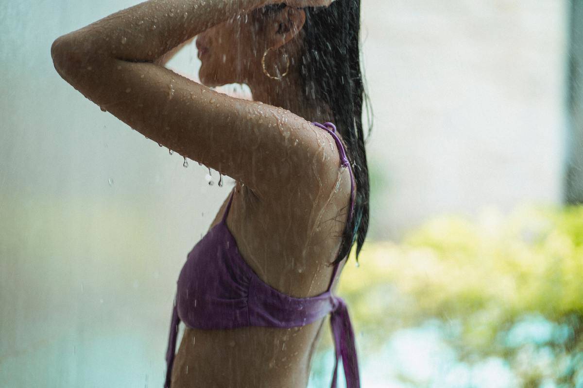 A woman in a purple bikini top under a shower.