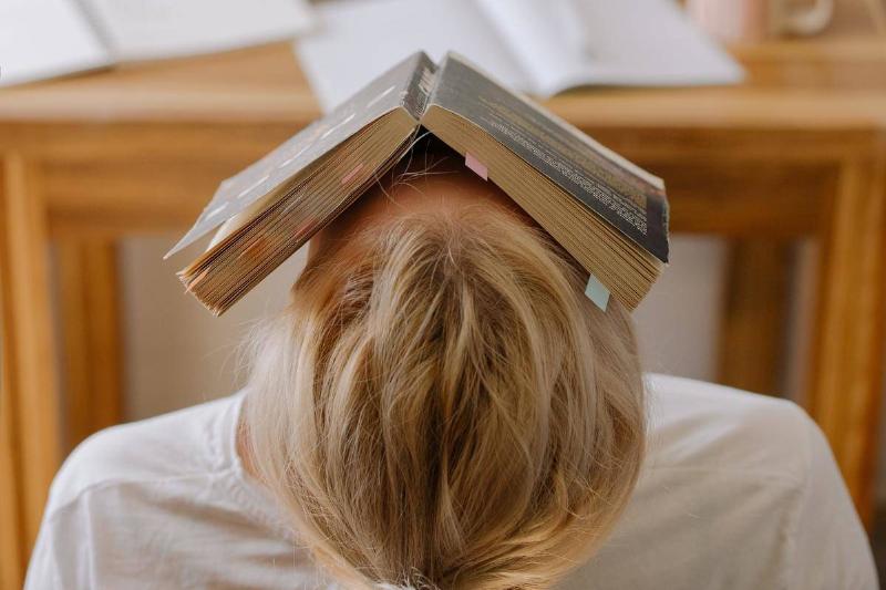 A woman leaning back in her seat with a book over her face.