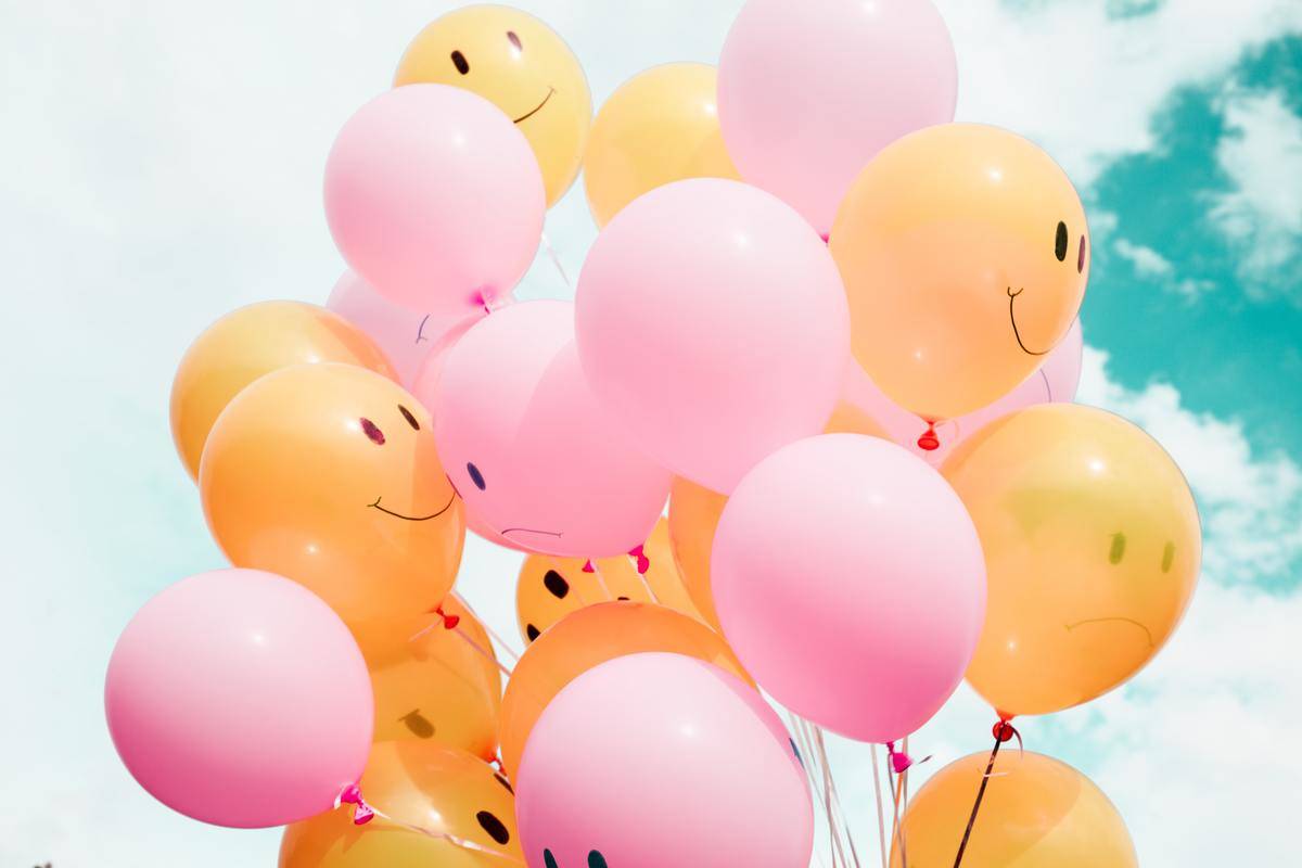 A bundle of pink and yellow balloons, the pink ones having sad faces and the yellow ones having happy faces.