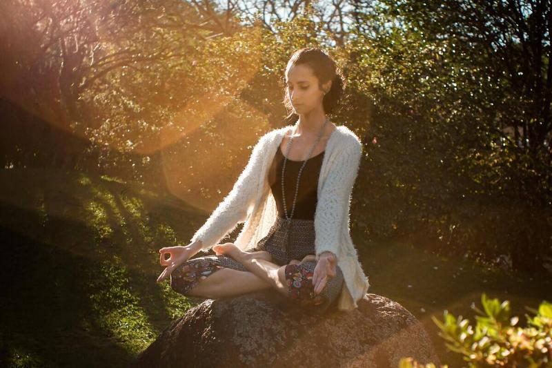 A woman meditating while sitting ona  rock in the middle of a garden.