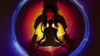 A woman sitting in a meditation pose with some colorful lights and rings being projected onto her body.