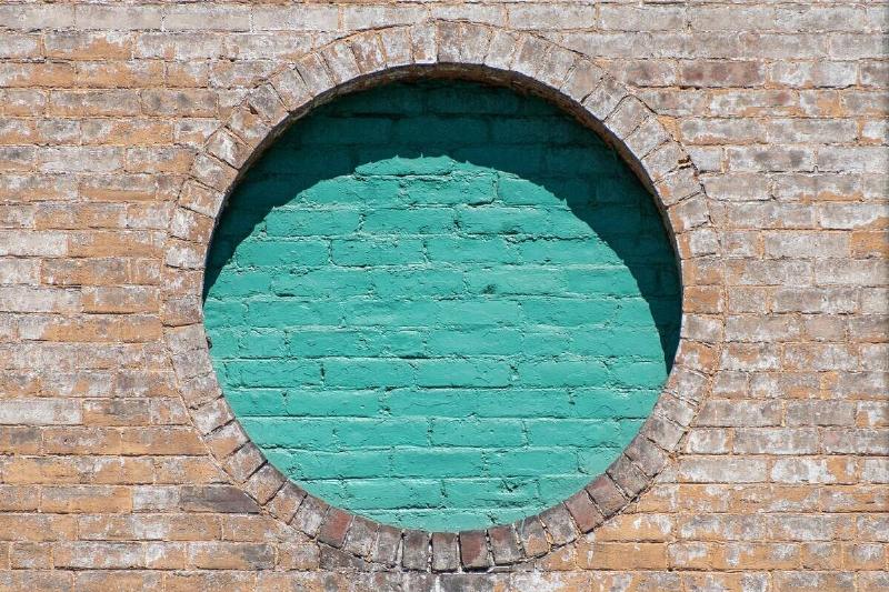 A brown brick wall with a circle of teal-painted bricks.