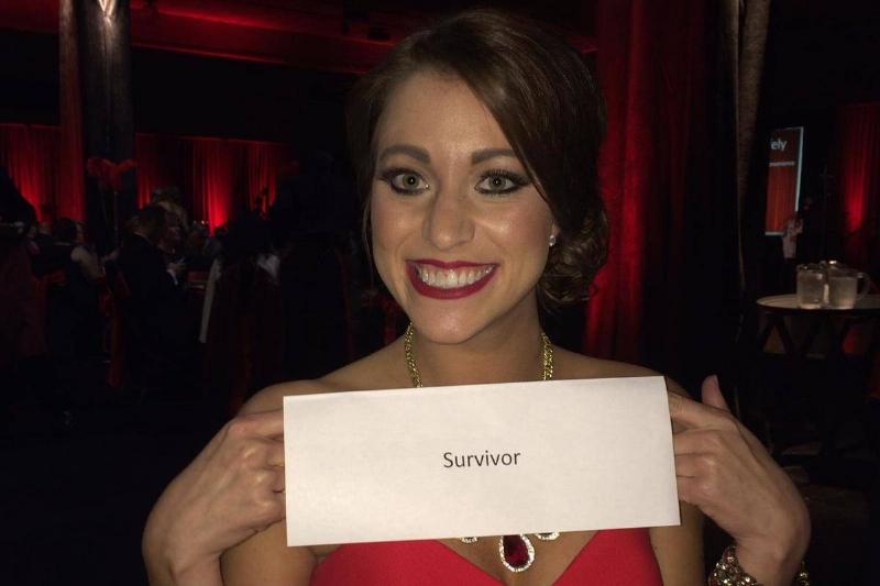 Brittany Williams at a banquet dinner, holding a sign that says 'survivor'.