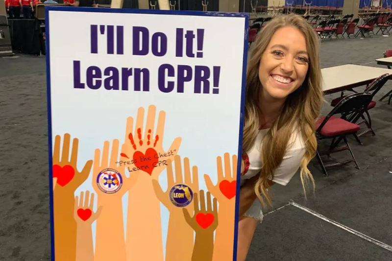 Brittany Williams standing by a sign encouraging people to learn CPR.