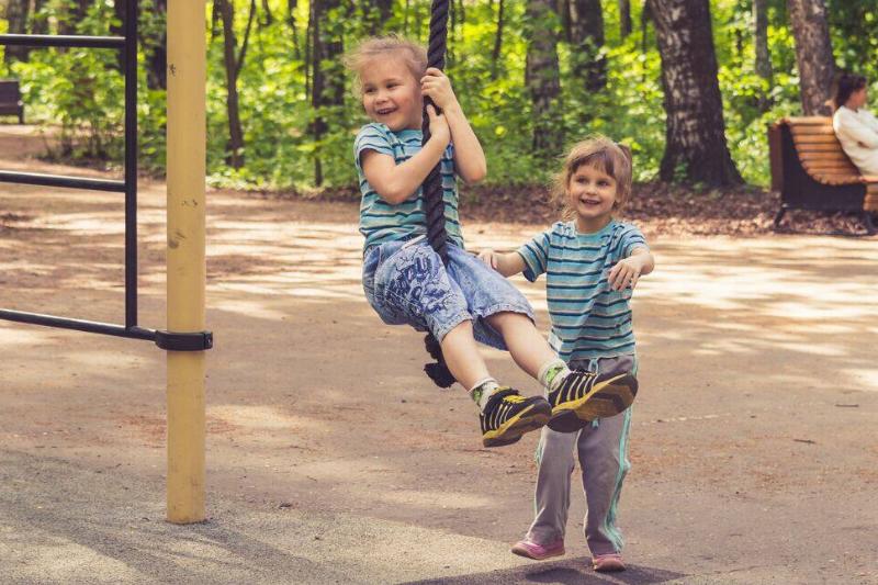 Two young childrens playing on a park rope.