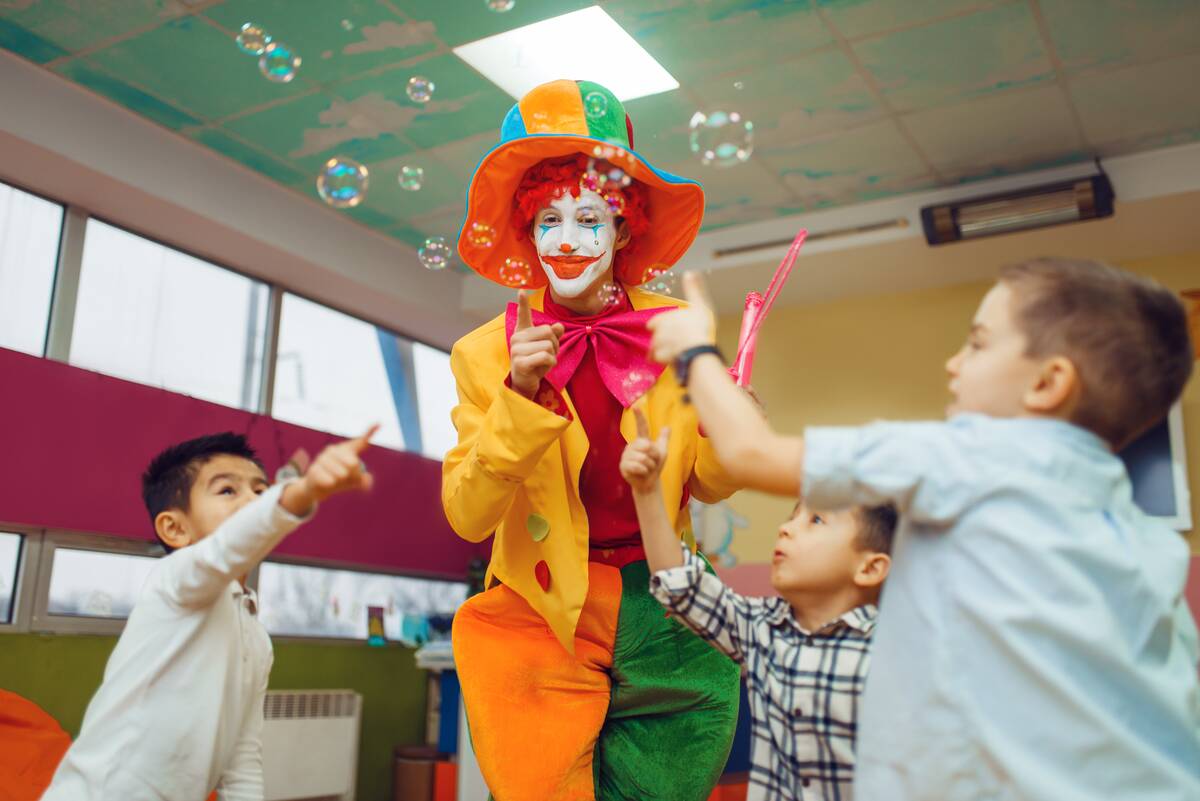 Funny clown with children inflates soap bubbles together.