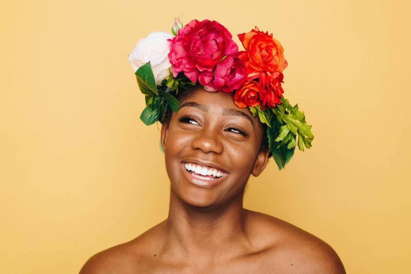 A woman smiling in front of a yellow background, wearing a bright crown of flowers.