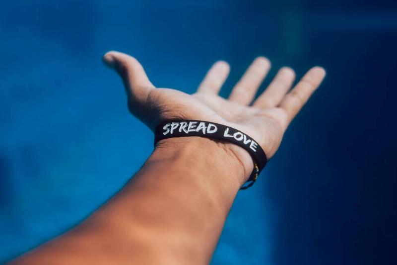Someone's hand reaching out and upward, their bracelet reading 'spread love'.