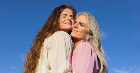 Two women hugging in front of a blue sky.
