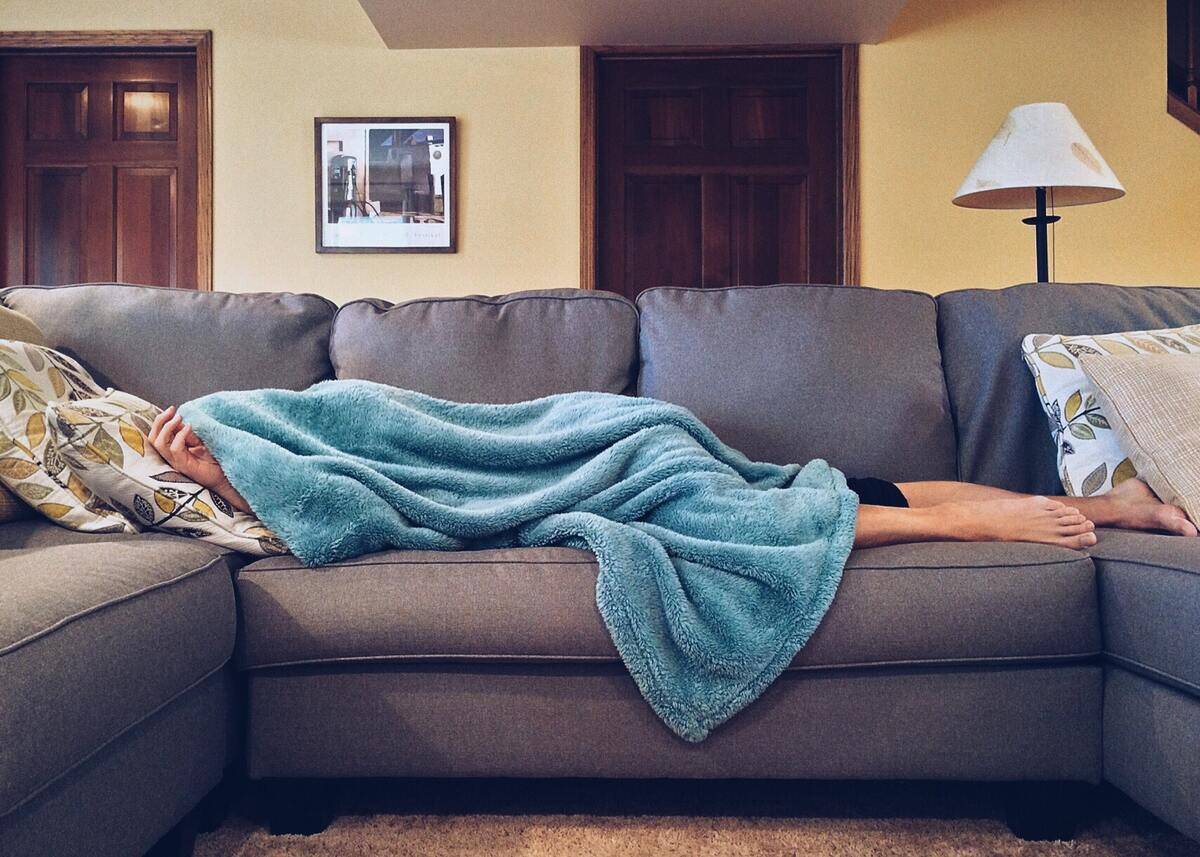 Someone asleep on their couch, covered in a blue blanket.